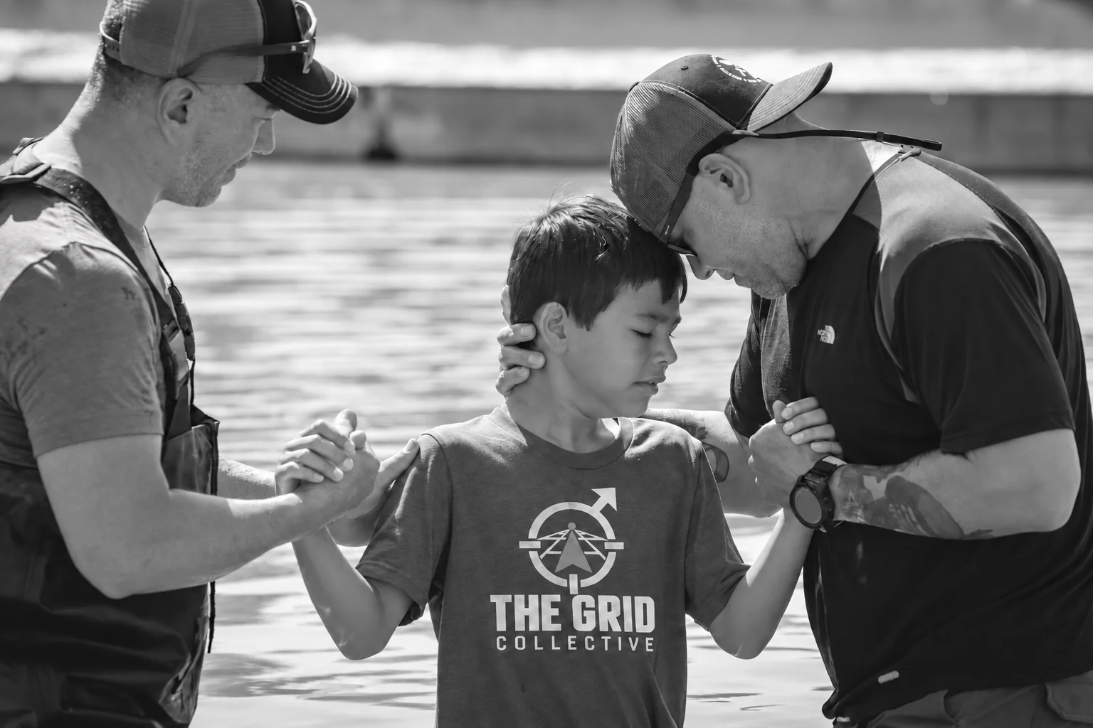 Two men praying with a boy during an outdoor baptism