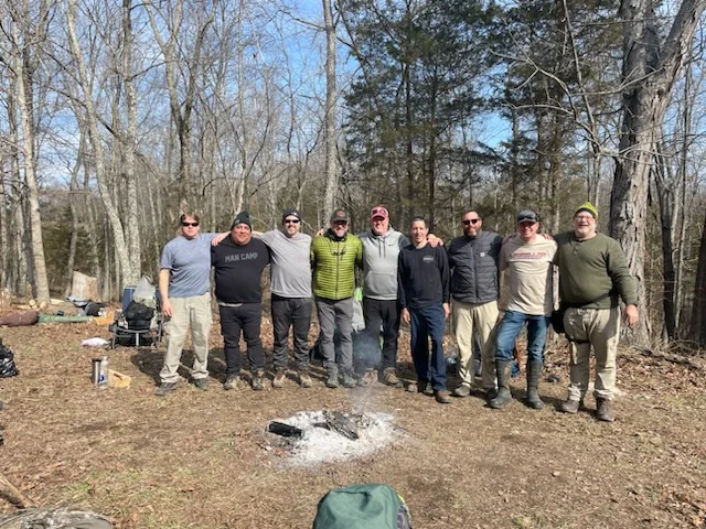 A group of men gathered together outdoors among the trees